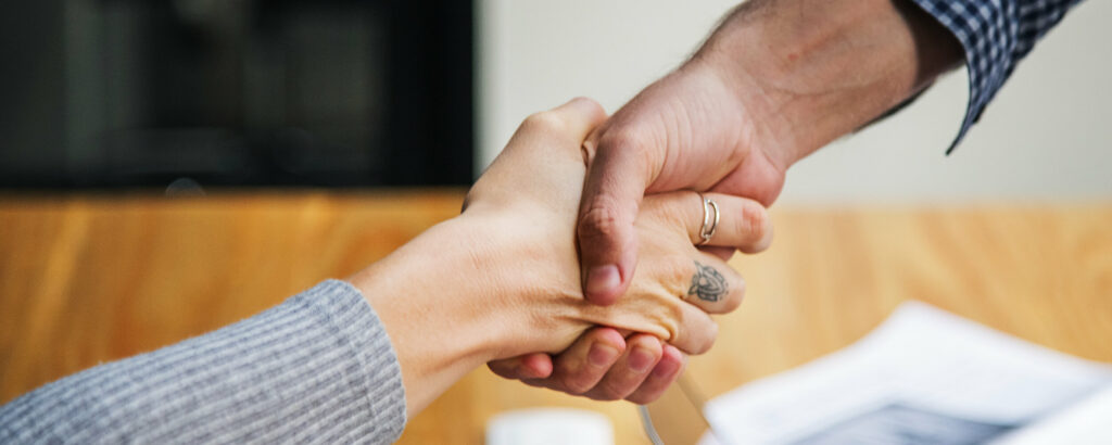 Deux personnes qui se serrent la main suite à une embauche. L'une d'entre elle vient de décrocher un emploi suite à sa reconversion.