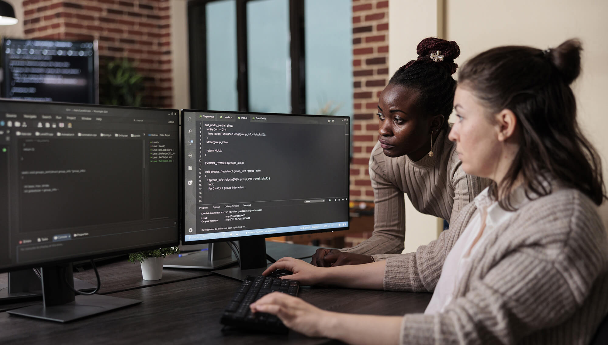 Sur la photo on voit deux femmes qui regarde des écrans d'ordinateur où se trouvent des lignes de code. Développeur web est un métier qui recrute.