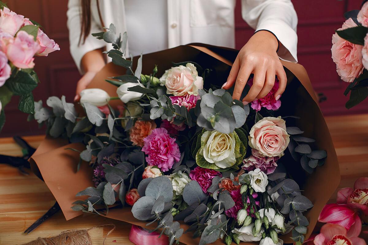 Un bouquet de fleurs est posé sur une table. La fleuriste est en train d'y apporter les derniers détails.