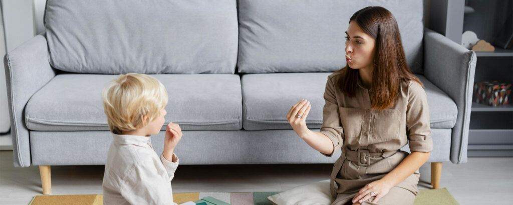 Une femme et un jeune garçon sont assis par terre. Elle lui fait faire ses exercices d'orthophonie.