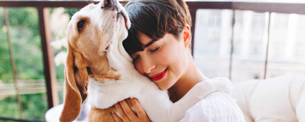 Une femme qui ferme les yeux et sourit fait un câlin à son chien. Il a mis ses pattes sur ses épaules et semble lui faire un câlin en retour.