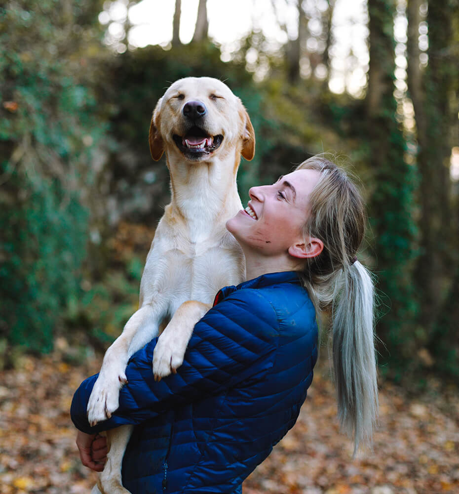 Une dogsitter souriante qui tient dans ses bras un chien qui semble sourire.